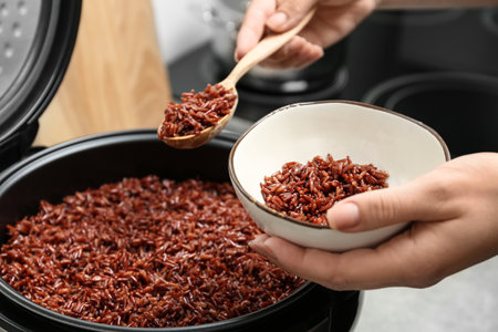 Woman putting brown rice into bowl from multi cooker in kitchen, closeupの写真素材