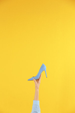 Woman holding classic high heeled shoe on yellow background, closeup. Space for textの写真素材