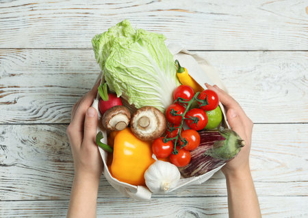 Woman holding bag full of fresh vegetables on wooden background, top viewの写真素材
