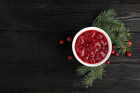 Bowl of cranberry sauce with fir tree branches on wooden background, flat lay. Space for textの写真素材
