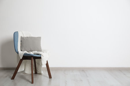 Stylish chair with pillow and plaid near white wall. Idea for interior designの写真素材