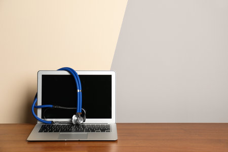 Modern laptop with stethoscope on table against color wall. Mockup for designの写真素材