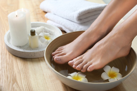 Closeup view of woman soaking her feet in dish with water and flowers on wooden floor. spa treatmentの写真素材