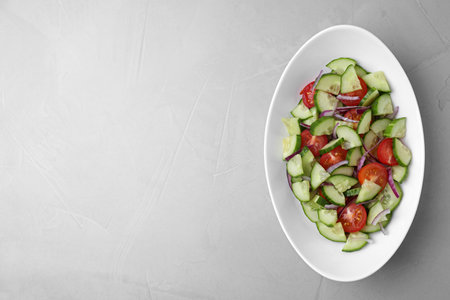 Plate of vegetarian salad with cucumber, tomato and onion on light background, top view. Space for textの写真素材