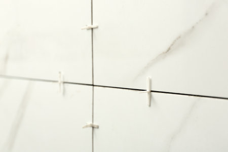 Closeup view of ceramic tiles with plastic crosses in joints on wall. Building and renovation worksの写真素材
