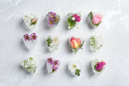 Heart shaped ice cubes with flowers on gray background, flat layの写真素材