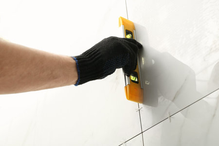 Man checking proper ceramic tile installation with level on wall, closeup. Building and renovation...