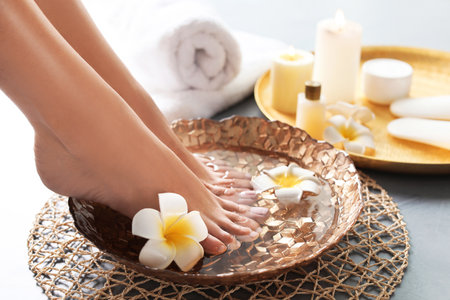 Closeup view of woman soaking her feet in dish with water and flowers on gray floor. spa treatmentの写真素材