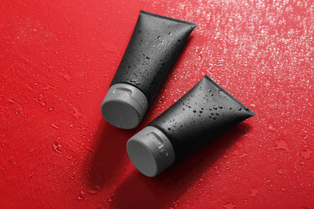 Black tubes on wet color surface, space for design. Men's cosmetic productsの写真素材