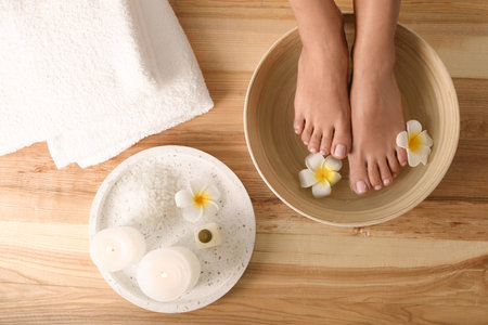 Woman soaking her feet in dish with water and flowers on wooden floor, top view. spa treatmentの写真素材