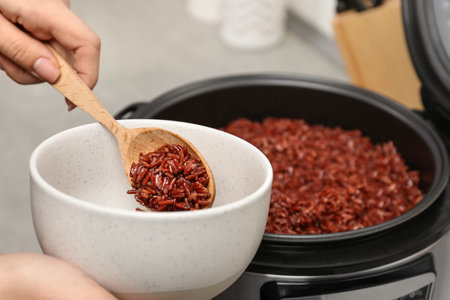 Woman putting brown rice into bowl from multi cooker in kitchen, closeupの写真素材