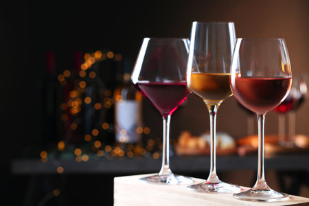 Glasses with different wines on wooden table against defocused lights. Space for textの写真素材