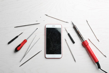 Mobile phone with broken display and repair tools on wooden table, flat layの写真素材