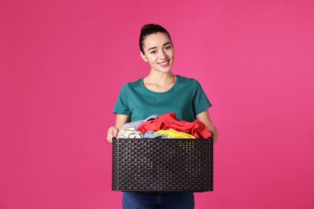 Happy young woman holding basket with clothes on color backgroundの写真素材