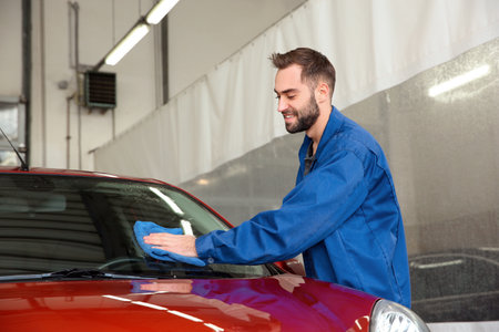 Worker cleaning automobile windshield with rag at car washの写真素材