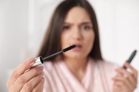Beautiful woman holding mascara brush with fallen eyelashes indoors, closeupの写真素材