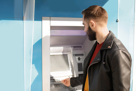 Young man taking money from cash machine outdoorsの写真素材