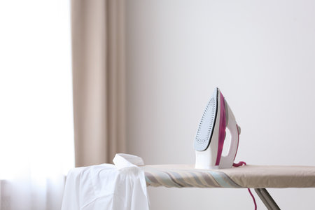 Modern iron and shirt on board in room. Space for textの写真素材