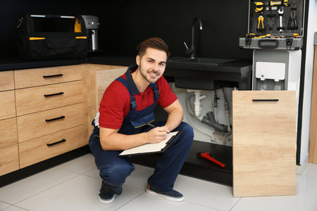 Male plumber with clipboard near kitchen sink. repair serviceの写真素材