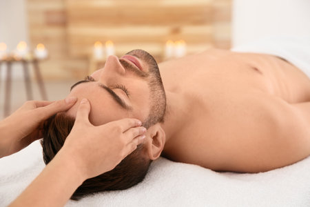 Handsome man receiving face massage in spa salonの写真素材