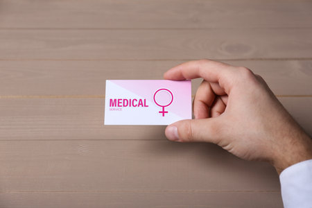 Man holding medical business card on wooden table, closeup. Women's health servicesの写真素材