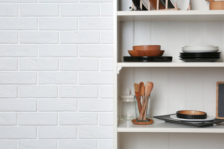 White shelving unit with set of dishware near brick wall. Space for textの写真素材