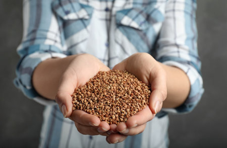 Woman holding raw buckwheat in hands on gray background, closeupの写真素材
