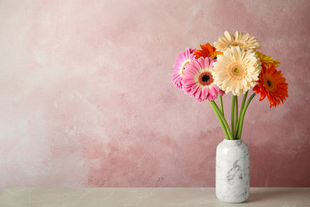 Bouquet of beautiful bright gerbera flowers in vase on marble table against color background. Space for textの写真素材