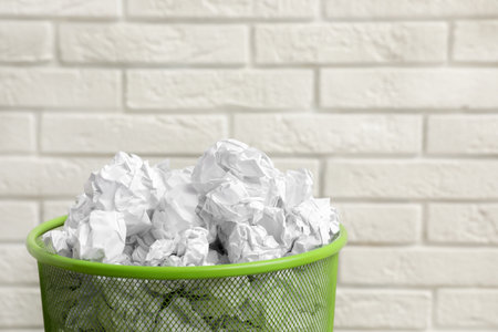 Metal bin with crumpled paper against brick wall, space for textの写真素材