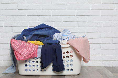 Laundry basket with dirty clothes on floor near brick wall. Space for textの写真素材
