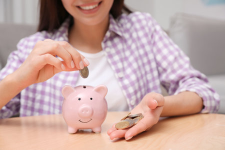 Happy woman putting coin into piggy bank at homeの写真素材