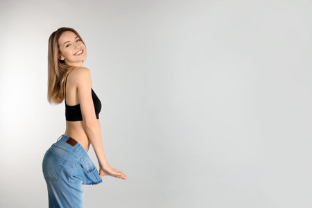 Slim woman in oversized jeans on light background, space for text. perfect bodyの写真素材