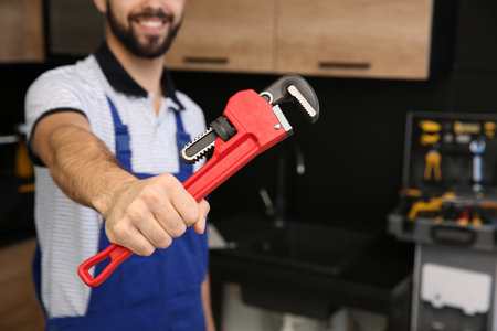 Male plumber holding pipe wrench in kitchen, closeup with space for text. repair serviceの写真素材