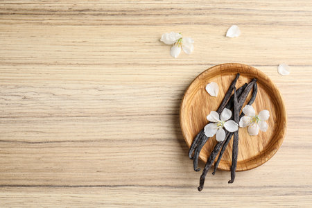 Flat lay composition with aromatic vanilla sticks and flowers on wooden background, space for text