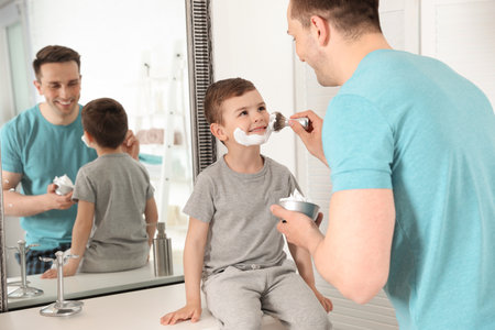 Dad applying shaving foam onto son's face in bathroomの写真素材