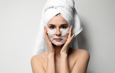 Beautiful woman with cotton face and eye masks against light backgroundの写真素材