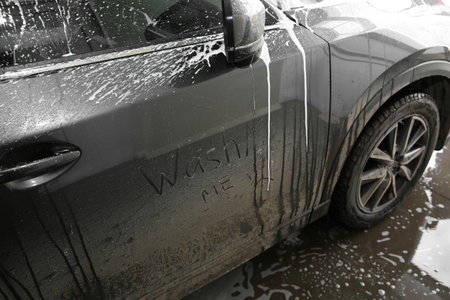 Inscription WASH ME and sad smiley on car door, closeup