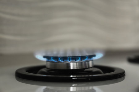 Gas burner with blue flame on modern stove, closeup. Space for text