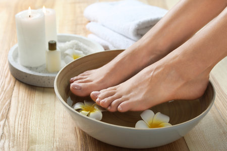 Closeup view of woman soaking her feet in dish with water and flowers on wooden floor. spa treatmentの写真素材
