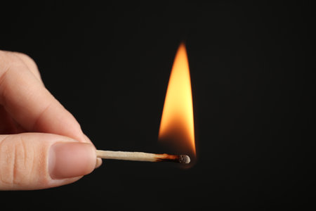 Woman holding burning match on black background, closeup. Space for textの写真素材