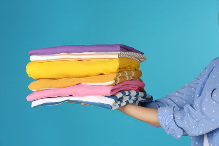 Young woman holding clean laundry on color background, closeup