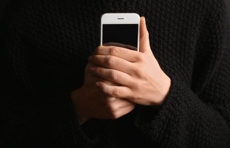 Lonely woman holding smartphone on black background, closeup