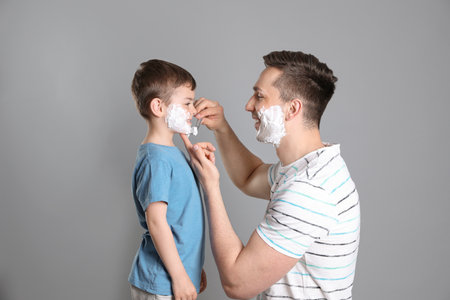 Dad pretending to shave his little son on color backgroundの写真素材