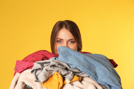 Young woman holding pile of dirty laundry on color backgroundの写真素材