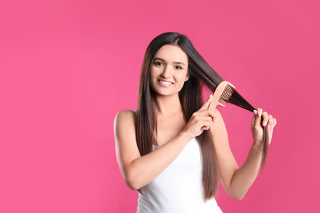 Beautiful smiling young woman with hair comb on color backgroundの写真素材