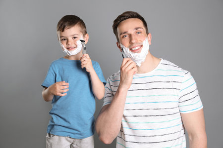 Dad shaving and little son imitating him on color backgroundの写真素材