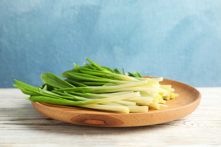 Wooden plate with wild garlic or ramson on table against color background. Space for text