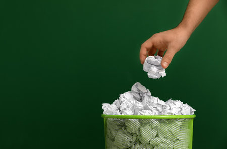 Woman throwing crumpled paper into metal bin on color background, closeup. Space for textの写真素材