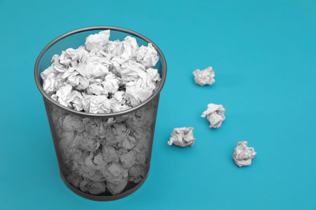 Metal bin with crumpled paper on color background, space for textの写真素材