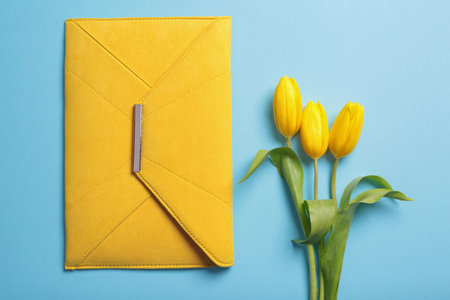 Flat lay composition with stylish woman's clutch and spring flowers on color background